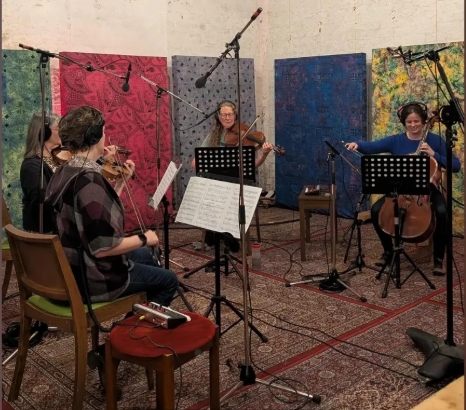 A group of four musicians playing string instruments in a recording studio, with colorful backdrops and music sheets on stands.